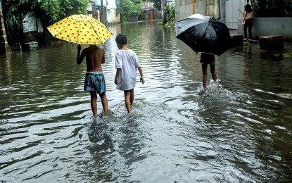 <p><strong>FROLIC.</strong> Children walk along a flooded street in San Francisco del Monte, Quezon City on June 11, 2023. Since leptospirosis is commonly acquired from rats’ urine mixed in the floodwater, the public is advised to wear proper gear such as boots. <em>(PNA photo by Joan Bondoc)</em></p>