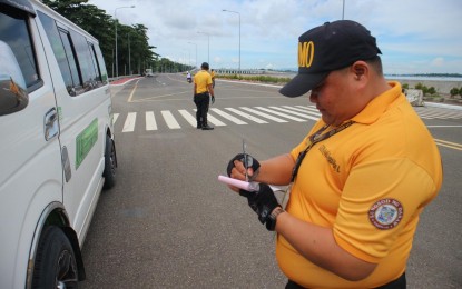 <p><strong>CITATION TICKET</strong>. Personnel from the City Traffic and Transportation Management Office (CTTMO) issues a citation ticket to a passenger van as it passes through the newly opened segment A of the Davao City Coastal Bypass Road on Monday (July 3, 2023).  The CTTMO warned the public utility vehicle drivers not to “cut trips” by passing through the new motorway.<em> (PNA photo by Robinson Niñal Jr.)</em></p>