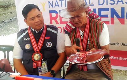 <p><strong>OFFERING.</strong> Albert Mogol, Office of Civil Defense (OCD)-Cordillera director and Cordillera Disaster Risk Reduction Management Council (CDRRMC) chairman, listens to a “mambunong” (native priest) explaining the symbolism of the bile from a butchered pig offering during the opening of the observance of National Disaster Resilience Month on Monday (July 10, 2023). The CDRRMC urged local government units and individuals to be ready for drought due to f El Niño and the possible occasional strong rains that might hit the region. <em>(PNA photo by Liza T. Agoot)</em></p>
