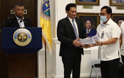 <p><strong>PROFITEERING CASE</strong>. Senior Deputy State Prosecutor Anthony Fadullon (center) receives a copy of the charge sheet from the National Bureau of Investigation at the Department of Justice in Manila on Monday (Sept. 18, 2023) in connection with onion hoarding charges against six individuals. Justice Secretary Jesus Crispin Remulla (left) also conducted a press conference. <em>(PNA photo by Benjamin Pulta)</em> </p>