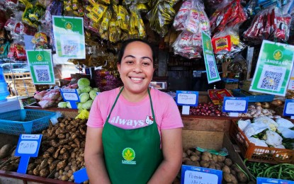 <p><strong>CASHLESS TRANSACTION</strong>. Iloilo Terminal Market vegetable stall owner Jasmin Marasigan now accepts cashless payments via QR code powered by LandBank. The Paleng-QR Ph Plus program aims to promote the use of QR PH, the national standard for electronic payments, through QR codes. <em>(Photo courtesy of LandBank)</em></p>