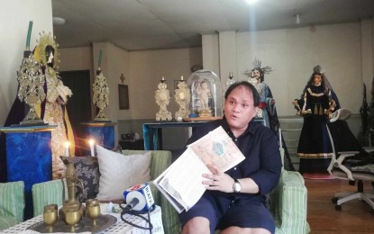 <p><strong>IMAGE CARETAKER</strong>. Image caretaker Niklaus de los Reyes Torres shows a print copy of his published “Garbed in Raiments of Light” digital book containing a collection of patterns in preparing vestments of saints in the Philippines. Torres, in an interview Wednesday (March 27, 2024), said that they also have to be mindful in communicating well to the public the stories of the saints in the Bible when preparing their vestments. <em>(PNA photo by Annabel Consuelo J. Petinglay</em>)</p>