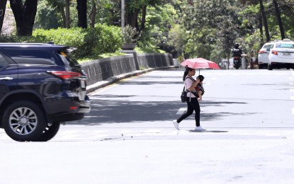 <p><strong>PROTECTED.</strong> A mother uses an umbrella to shield her toddler from the afternoon heat as they cross the intersection of Senator Miriam P. Defensor-Santiago and Quezon Avenues in Quezon City on Black Saturday (March 30, 2024). The heat index level in the city reached the "extreme caution" level of 38 to 39 degrees Celsius during the weekend. <em>(PNA photo by Robert Oswald P. Alfiler)</em></p>