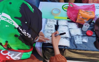 <p><strong>BUSTED.</strong> A female undercover agent documents the illegal drugs seized from four suspected drug peddlers during a drug buy-bust operation in Cotabato City on Thursday afternoon (April 18, 2024). Two of the arrested suspects were minors who were turned over to the city social service office.<em> (PDEA-BARMM photo)</em></p>