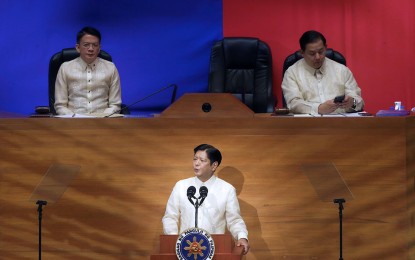 <p><strong>NATION LISTENS.</strong> President Ferdinand R. Marcos Jr. delivers his third State of the Nation Address at Batasang Pambansa in Quezon City on Monday (July 22, 2024), with Senate President Francis Escudero (left) and House of Representatives Speaker Martin Romualdez on stage. Marcos has prioritized the establishment of specialty hospitals, health centers, and mobile clinics to bring quality health services to the poor.<em> (PNA photo by Joan Bondoc)</em></p>