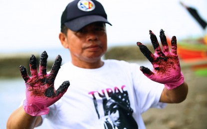 <p><strong>OIL SPILL.</strong> Danilo Canete, a fisher from Tanza, Cavite, shows his hands covered in oil residue in this photo taken on the shore of the coastal Barangay Amaya 5. Various villages in Ternate, Maragondon, Naic and parts of Tanza were affected. <em>(PNA photo by Joan Bondoc)</em></p>